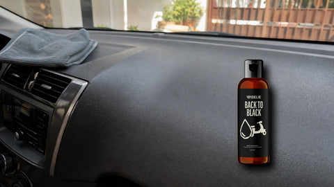 Dashboard mobil hitam yang tampak kusam dan berdebu dengan packshot Wiselie Back To Black untuk perawatan plastik kendaraan sesuai label